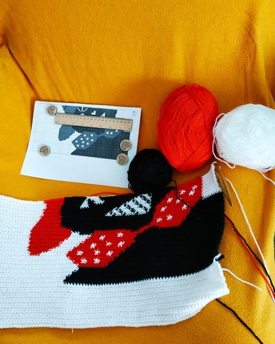 Work in progress beside the chart and balls of red, black and white yarn
